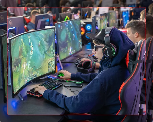 Un ragazzo con le cuffie e una felpa con cappuccio gioca concentrato davanti a un monitor curvo durante un torneo di eSport
